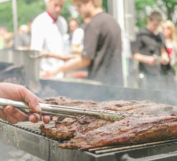 An individual grilling meat on a barbecue, showcasing culinary expertise in a sunny outdoor setting.