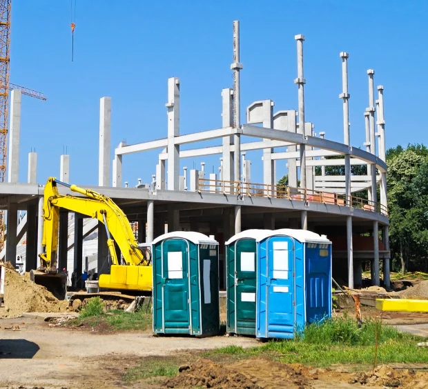 A construction site scene with a building under construction, highlighting portable toilets situated at the site.